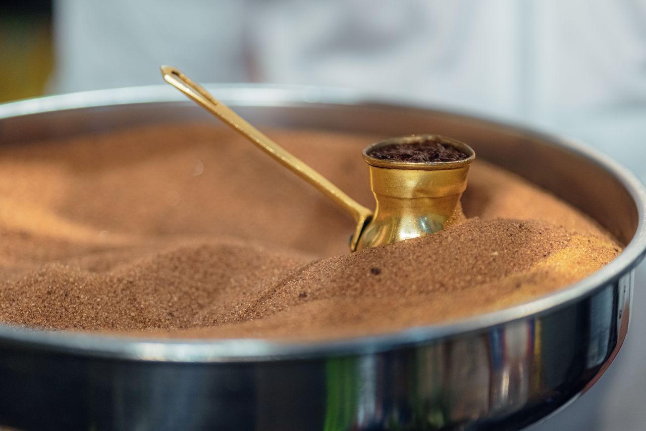 Close-up of Turkish coffee brewing in a cezve placed in heated sand at a cafe.
